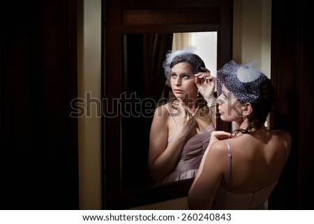 Beautiful lady in veil is looking at the mirror.