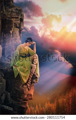 Lonely sad princess is sitting on the rock. Sunset mountains in the background.
