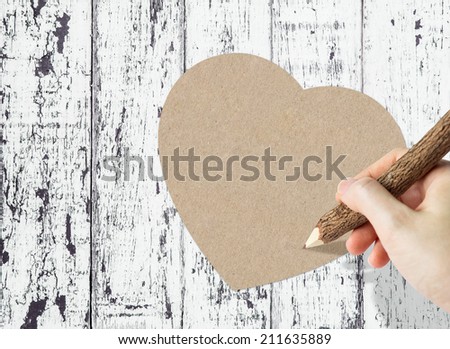 Woman hand writing paper heart on wooden background