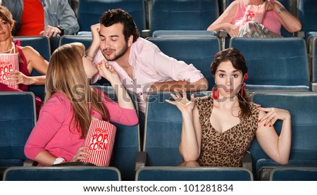 Man flirting with girl next to embarrassed friend in theater