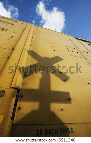 Shadow of a railroad crossing sign cast against the yellow side of a freight train car.