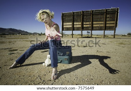 Woman sitting on suitcases in front of an old billboard reaching to the camera