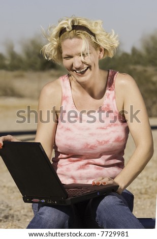 Laughing blonde woman outdoors with a laptop computer.