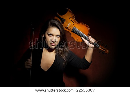 Pretty Hispanic woman in studio with violin raised above her head