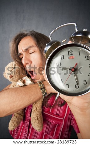 Sleepy handsome young man with long hair and alarm clock