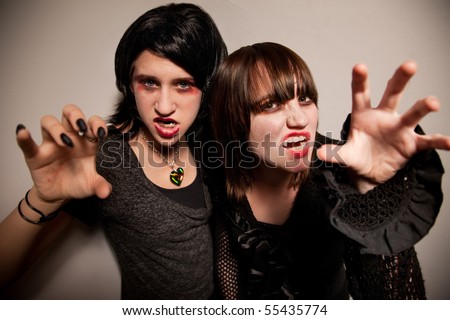 Two young vampire girls with sharp fangs reaching towards the camera
