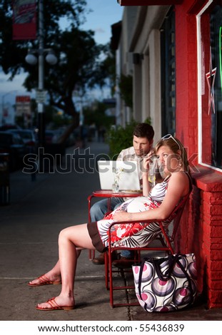 Pregnant woman sitting outside with annoying partner on computer next to her