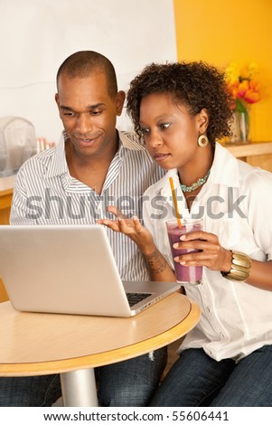 Two people at a cafe drinking frozen beverages and using a laptop. Vertical shot.