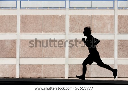Man in the shadows of building runs for exercise.