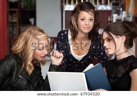 Three female college students studying with a book and laptop in a cafe