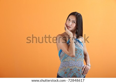 Young Mexican American woman on an orange background with palm on chin