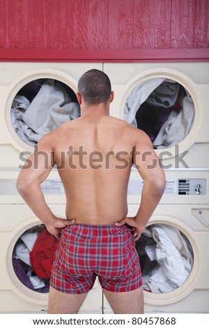 Muscular man in boxer shorts waits in front of washing machines
