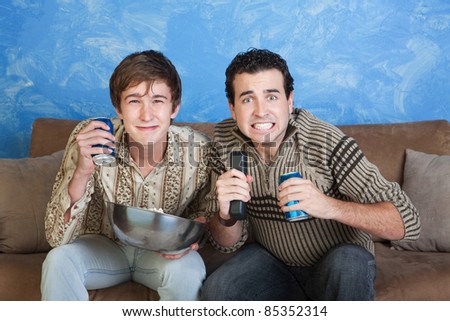 Two excited friends watch television with soda and bowl of popcorn