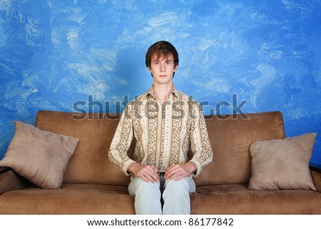 Young Caucasian man sits straight on sofa