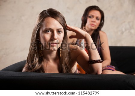Annoyed woman turns her head away from lady on sofa