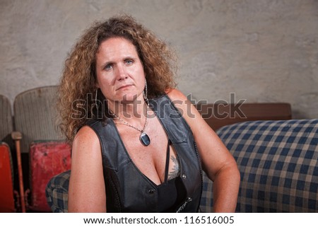 Serious mature biker woman in leather vest sitting indoors