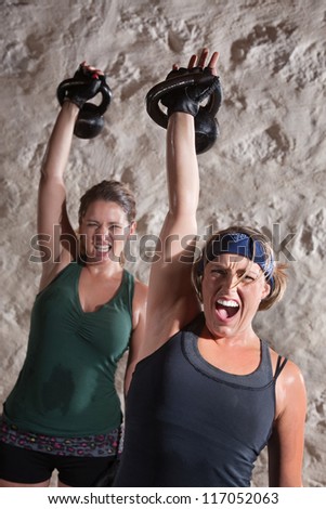 Intense women shout as they push kettle bell weights up