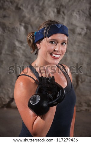 Smiling young woman sweating and lifting a kettle bell weights