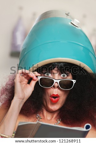 Surprised female reading magazine while under hair dryer