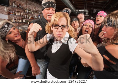 Brave nerd lady with fists up among laughing biker gang
