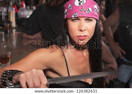 Frowning tough female gang member displaying a dagger