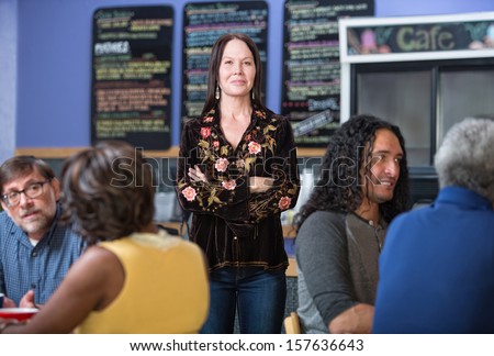 Cheerful woman standing in group of customers in cafe