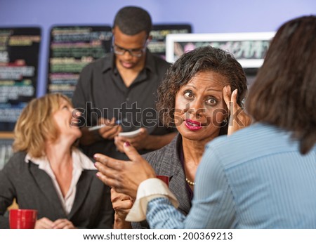 Woman with fingers on head listening to friend in cafe