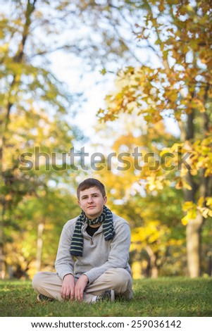 Calm Caucasian teenager sitting on grass during the  autumn season