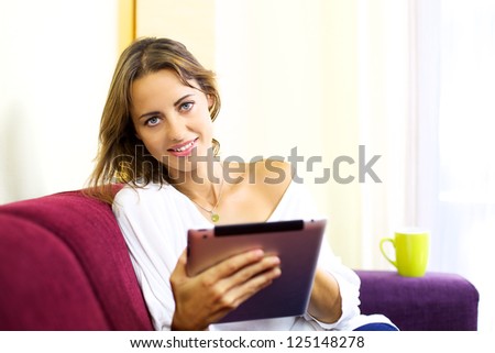 Good looking female model smiling while surfing the web relaxing at home on sofa