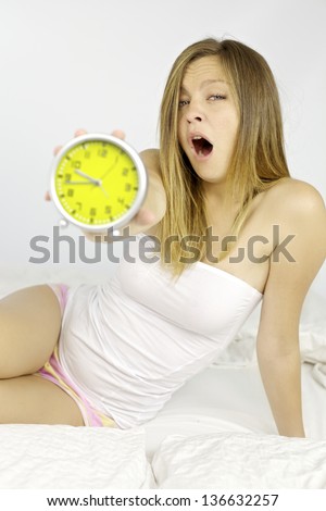 Sleepy blond woman in bed showing alarm clock not ready to go to work tired