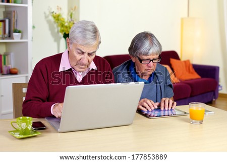 Two old people working with a computer and a tablet.