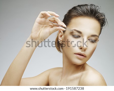 Beautiful young woman plucking eyebrows