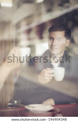 Thoughtful  adult man with coffee cup looking through window in cafe