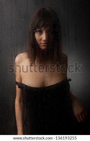The brunette in a black dress for a wet glass on a black background.