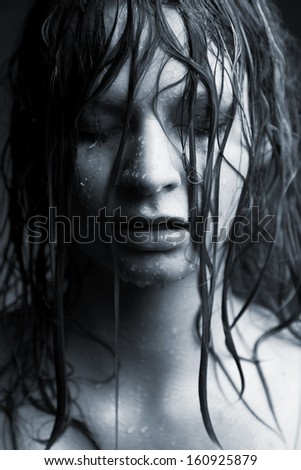 Portrait of a girl with wet hair, the face of which the water flows, on a dark background.