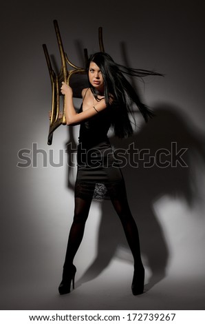 Beautiful leggy brunette girl with fluttering hair defends using the chair on a gray background.
