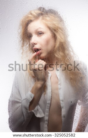 Beautiful blonde in a white shirt for a wet glass on a gray background.
