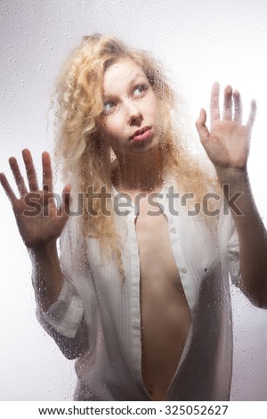 Beautiful blonde in a white shirt for a wet glass on a gray background.