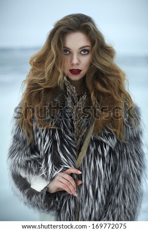 stylish blond girl with bright makeup, near the sea in winter, in a luxurious fur coat