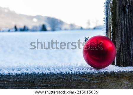 a shiny red christmas ball resting on a wooden fence covered with hoarfrost ice crystals