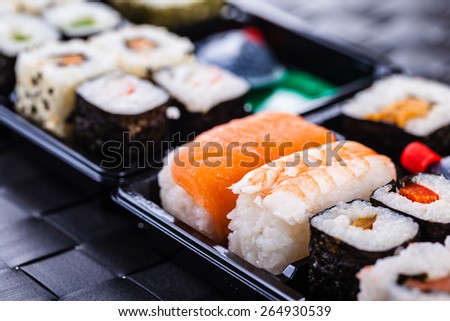 a sushi box or bento box with assorted sushi pieces over a dark black lunch mat