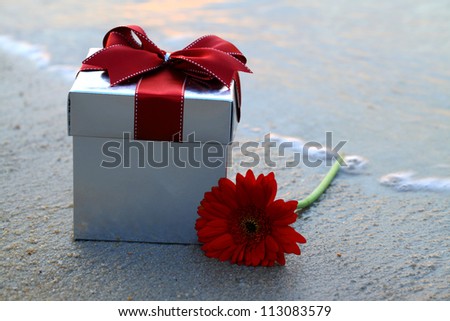A gift box and a daisy flower put on the beach.