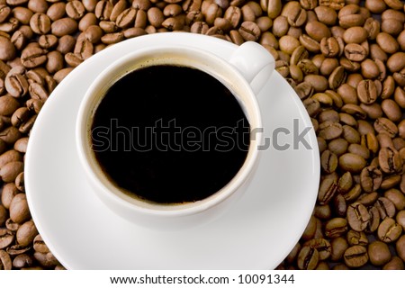 Cup filled with black coffee top view and coffee beans in the background