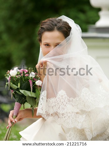 Bride hiding behind her veil, smiling happily and coyly.