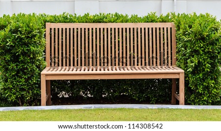 Wooden Bench in Green Bush in front of White Wall.