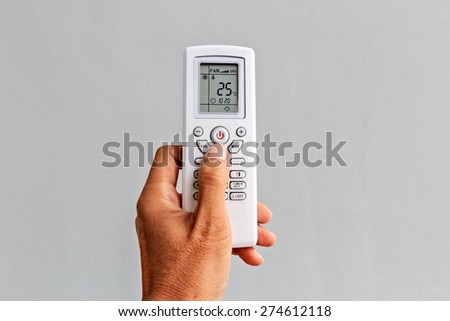 Left Hand holds a Remote Control of Air conditioner on grey background