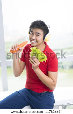 Vertical portrait of a cool vegetarian enjoying music and singing along using a carrot as a mic