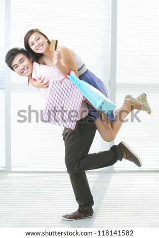 Energetic guy carrying his girlfriend on the back after shopping with a credit card