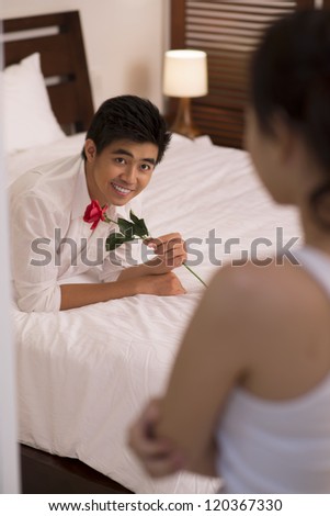 Portrait of young Asian man with rose lying on bed and looking at his girlfriend