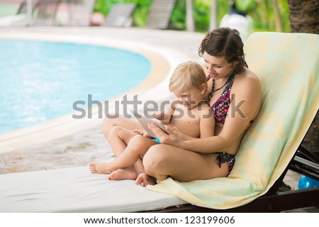 Family of two resting by the pool interested in what is shown on the tablet screen